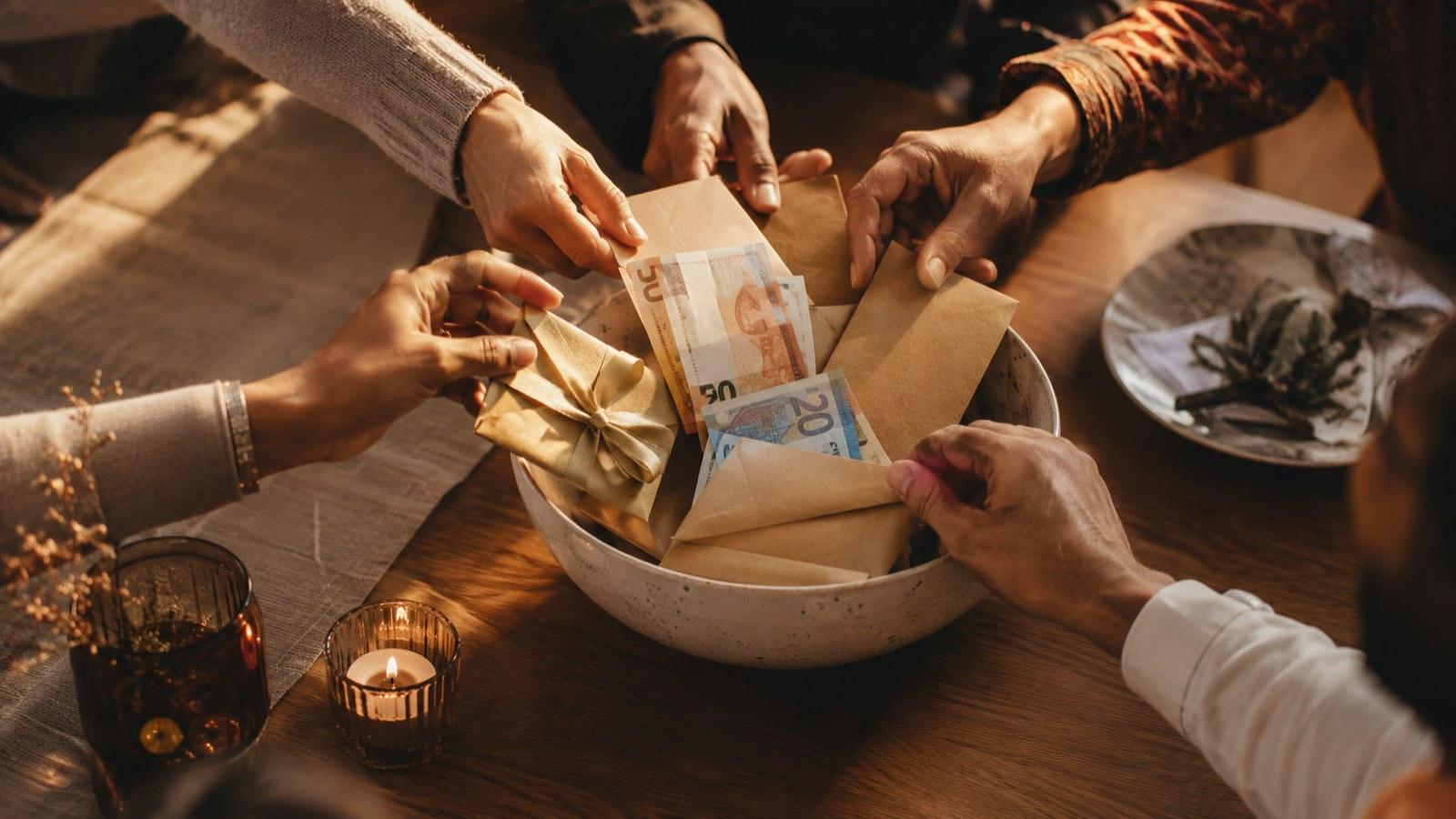 Des mains de tous âges déposent des enveloppes dans un pot commun, à la lumière des bougies